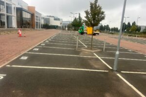 Freshly painted white parking bay lines on a tarmac car park beside block paving