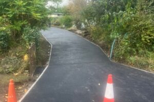 Newly laid long tarmac driveway through trees with traffic cones
